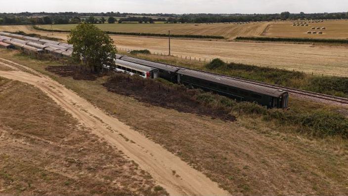 Trains stationed along tracks in the middle of farmland, with hay bales in the distance.
