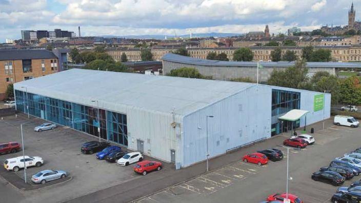 A wide grey gym building surrounded by a car park.