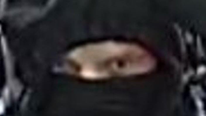 The eyes of a person stare out from behind a black face covering