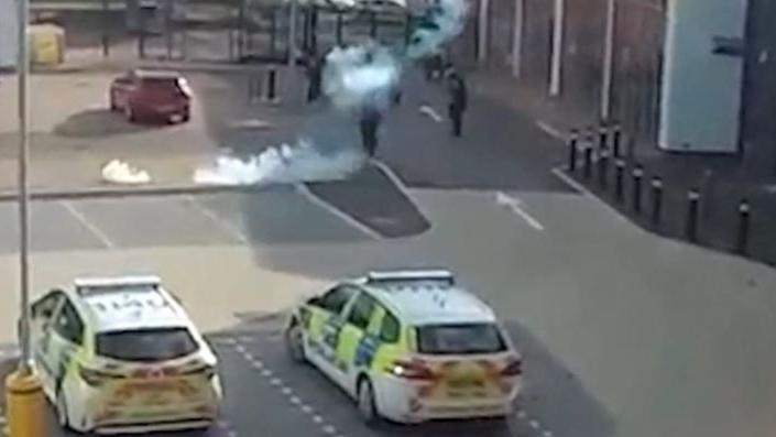 A screen grab of the police footage which shows a smoke from a stun grenade and two police cars in the foreground.