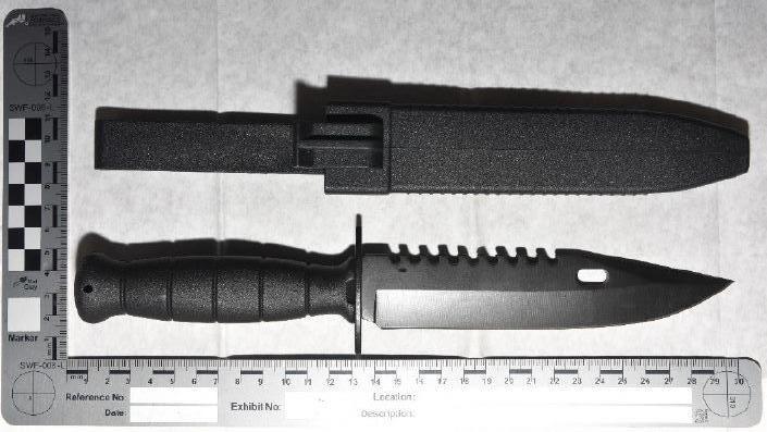 A knife with a black handle and a sharp point. It has a ridged edge on part of the blade. It is next to an evidence ruler.