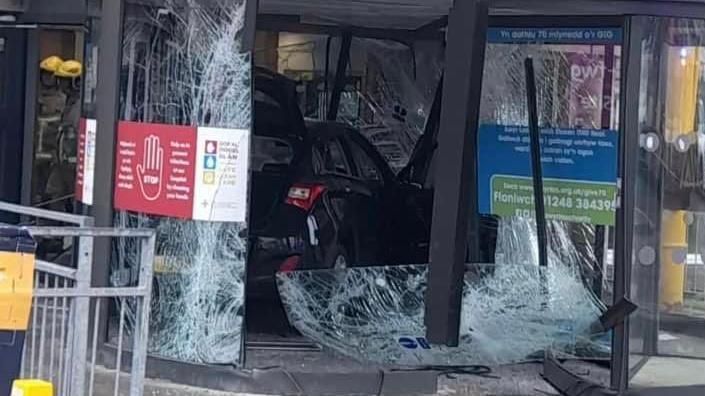 Car in front entrance of hospital and smashed entrance doors