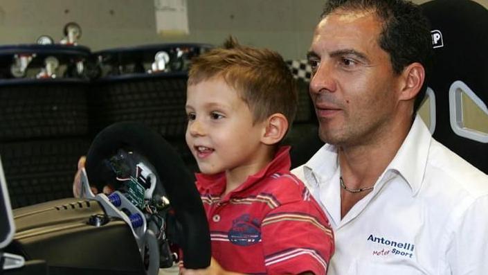 A picture of Kimi Antonelli, aged about five or six, sat on his dad Marco's knee and holding a steering wheel while playing on a motor racing simulator. Kimi has an excited expression on his face 