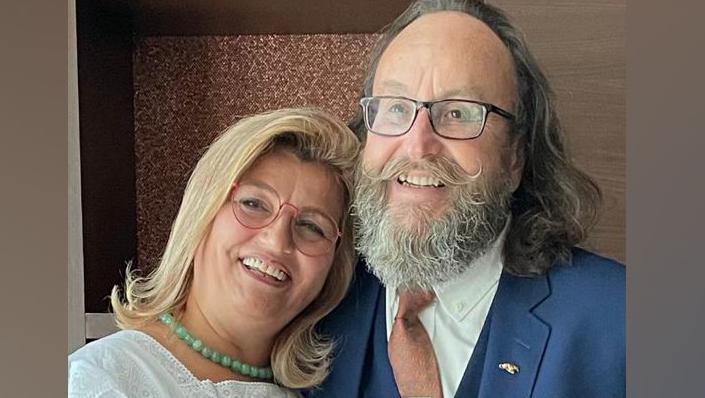 Lili and Dave Myers. Lili is leaning her head on Dave's shoulder an both are smiling. Lili has blonde, shoulder-length hair and a pale jade-green bead necklace. Dave is wearing a royal blue suit with salmon pink tie, with gold tie pin. He has shoulder length dark grey hair and his trademark full beard and moustache.