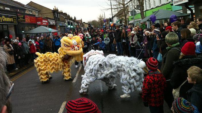 A Chinese lion dance is taking place on a busy street. There are crowds of people watching the performance