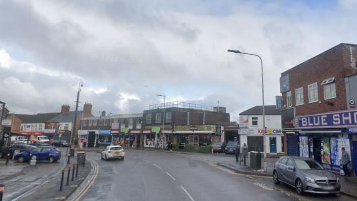 Lincoln Road, Peterborough, at the junction with Alma Road on the right. The road is bending to the left. It shows two storey buildings with shop fronts.