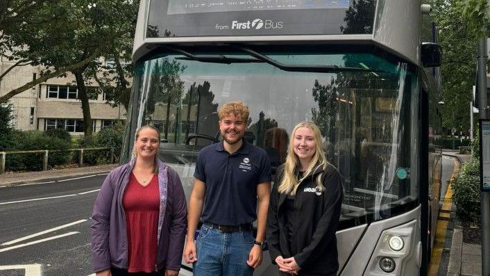 Two women and a man standing in front of a grey Norwich electric First Bus