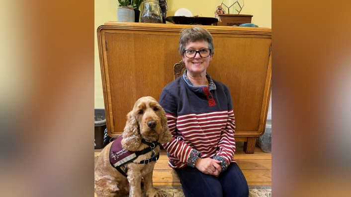 Abingdon resident Sonya Paige, who lost all her hearing when she was 30, and her hearing dog Barkley at home. She is smiling for the camera while kneeling next to Barkley.