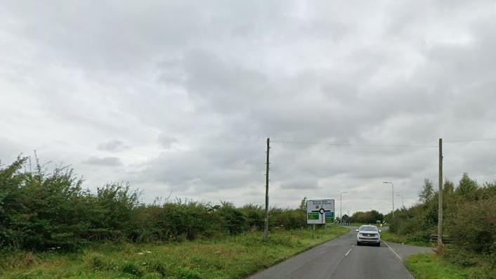 A general view of Burgh Road, off which the development would be built. It is a single carriage rural road flanked by hedges.