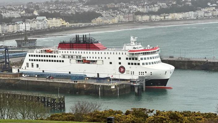 The Manxman ferry, which is a large vessel in the Steam Packet's livery of white, red and black. It is moored in Douglas Harbour with the sweep of Douglas Promenade behind it in the background.