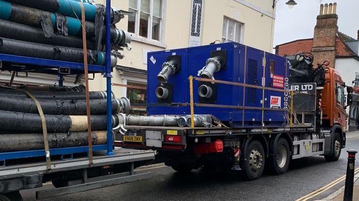 A lorry carrying pipes delivers equipment to the street