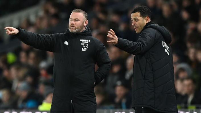 Wayne Rooney and Liam Rosenior on the touchline wearing black Derby County team coats