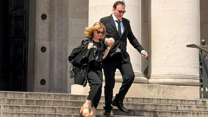 Quentin Tarantino and Kylie Minogue outside National Museum Cardiff. They are walking down the steps outside the museum holding hands. They are both wearing all black outfits and sunglasses. Kylie has a pair of brown tan high heels on.
