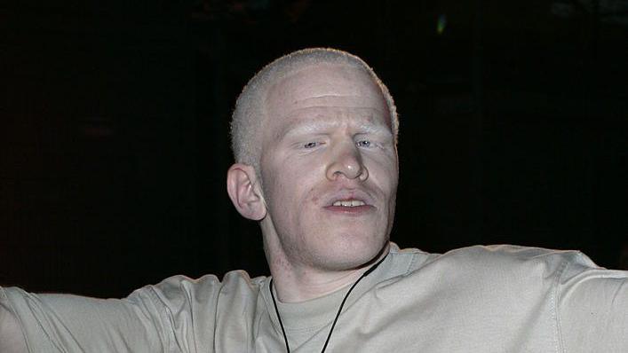 Darnell Swallow looks at the camera before he enters the Big Brother House. He wears a grey T-shirt and spreads his arms out from his body. He wears a microphone around his neck. 
