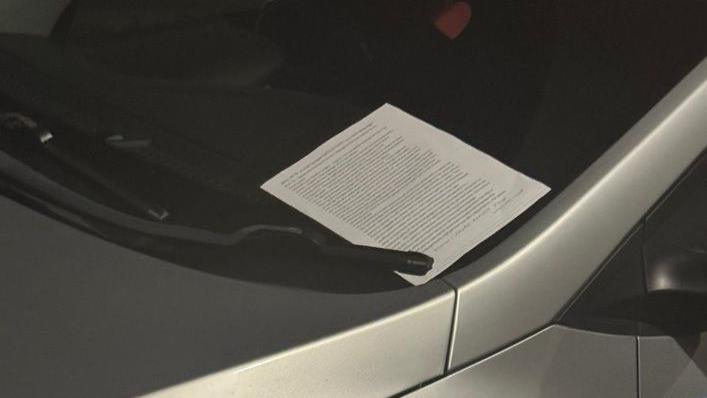 A flyer placed on the windscreen of a vehicle. It is held down by a windscreen wiper