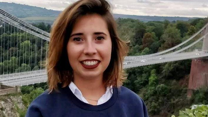 Photo of Marta Elena Vento infront of a bridge over a gorge, smiling to camera