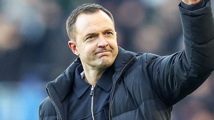 Birmingham City boss Chris Davies punching the air with his left fist while wearing a blue coast and blue zip tracksuit top
