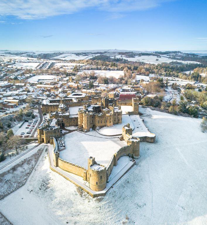 Aerial view of a yellow-stoned castle and town covered in snow beneath a blue sky