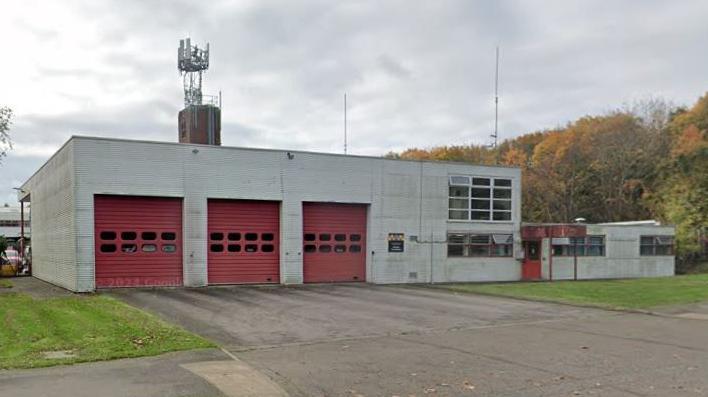 A single storey 1970s fire station at Moulton Road station in Northampton. It is a white building with there red doors to fire engine bays. 