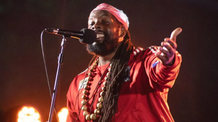 Singer Da Fuchaman smiling and performing on stage, with his arm outstretched