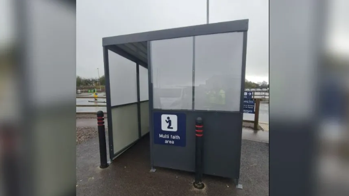 Grey multi faith area that is shaped similar to a bus stop in Bristol Airport's car park on grey day.