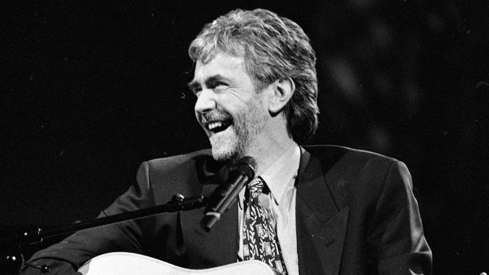 Charlie McGettigan sitting holding a guitar and smiling in front of a microphone