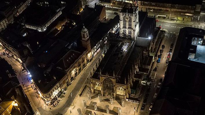 A bird's view of Hull Minster at night. It shows a t-shaped building illuminated by lights.