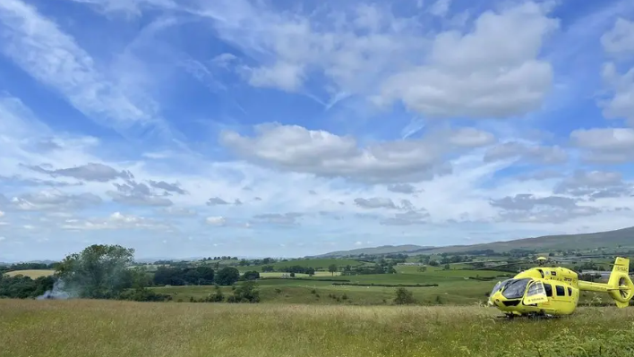 An air ambulance lands in a field with smoke in the background