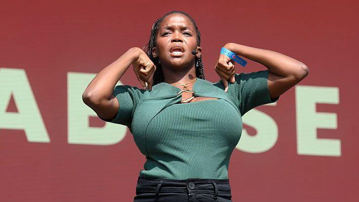 Oti Mabuse wearing a green shirt and black jeans is shown part-way through leading her fitness class at the festival.