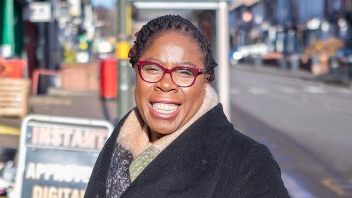 Paulette Hamilton wearing a black coat and multi-colours scarf in a high street