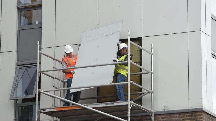 Image showing two workmen in white hardhats and hi-vis vests removing external cladding from Burnham Tower on the Chalcots Estate in Camden in 2017