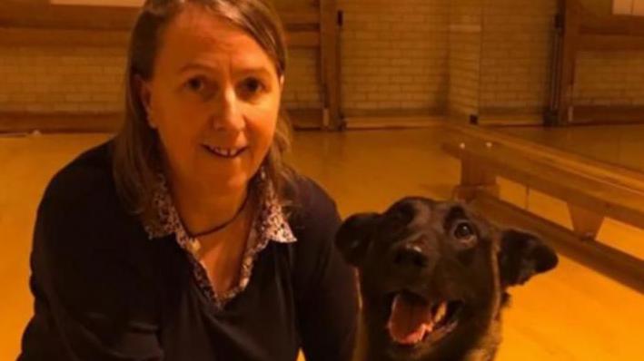 Mandy, a woman with brown hair and a navy cardigan sitting next to her dog, who appears to be smiling