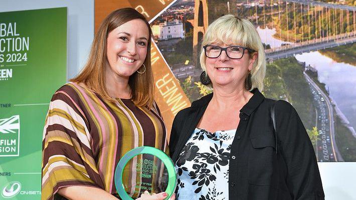 Two women smiling at the camera holding an award 