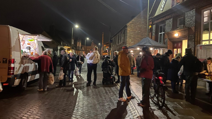 A crowd of people outside queueing for food