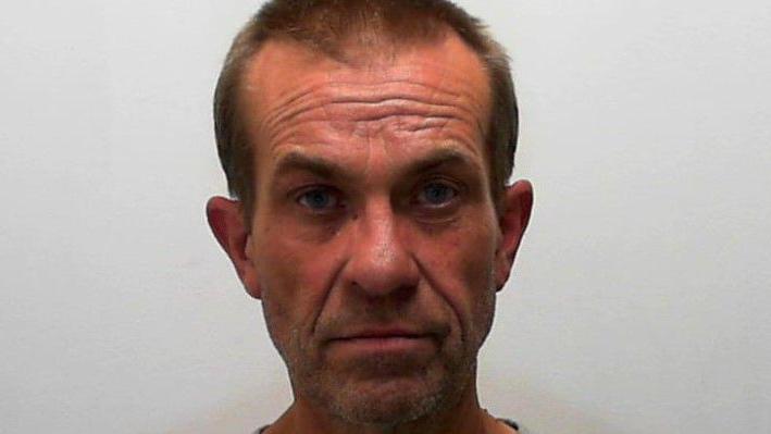 A police mugshot of Stephen Carr. He has close cropped, light brown hair which is receding above his temples and dark stubble on his chin.