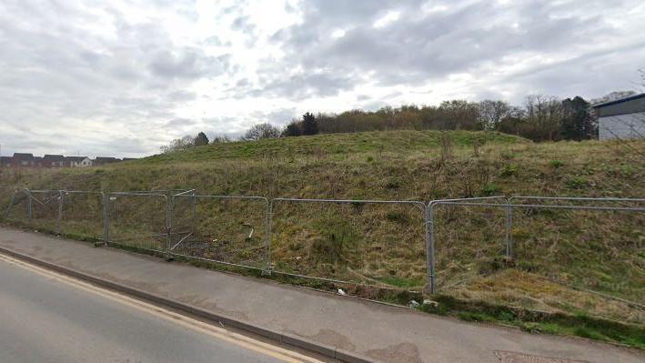 Picture of field with tall metal fencing surrounding it at the edge of a road