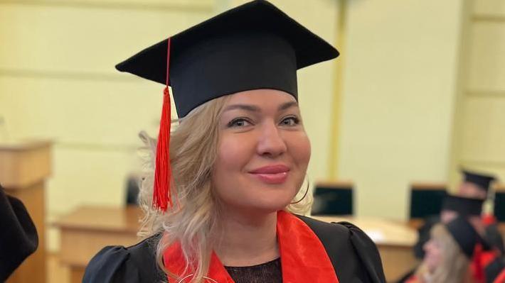 Dr Olga Pantas in a graduation outfit - she wears academic robes and board, smiling towards camera.