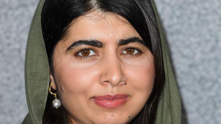 A close-up headshot of Malala Yousafzai who has dark hair and is wearing a dark green head scarf.