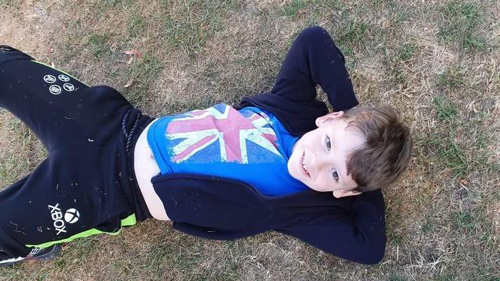 Lennix Sutcliffe pictured lying on his back on grass, with his hands behind his head, smiling at the camera. He wears a dark hoodie over a blue t-shirt with the union jack on it, and black and green jogging bottoms with the Xbox logo on them. 