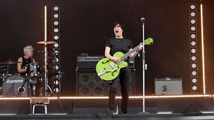 Sharleen stands on stage with a bright green guitar. She is singing with other members of the band behind her and word "Texas" above the stage.