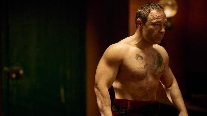 Steven Graham looking pensive and focused ahead of a boxing match. He has a tattoo of a woman and one of a bird on his chest.