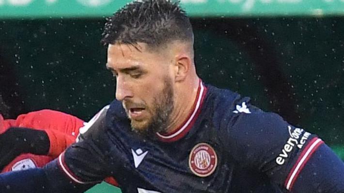Dan Sweeney in dark blue Stevenage shirt trying to get ahead of a red-shirted Barnsley player