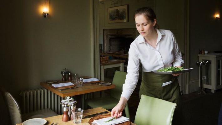 Woman wearing apron setting table in a restaurant