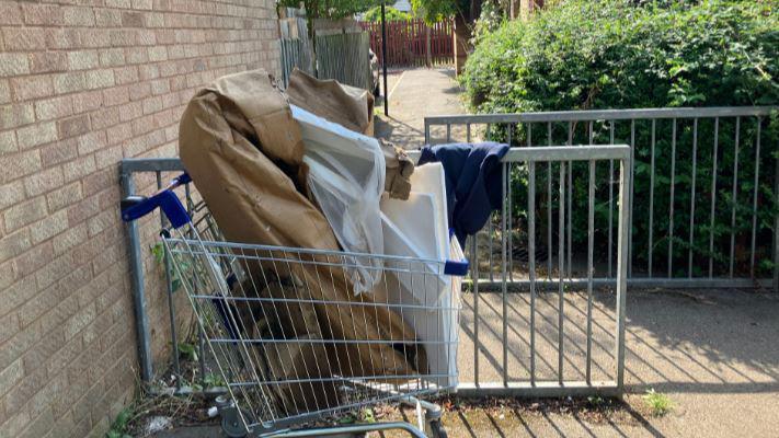 A trolley abandoned with rubbish in it- placed by the gates of a walkway