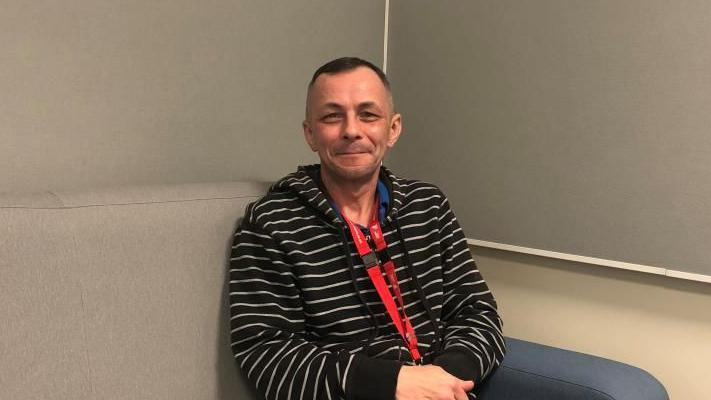 Dr Granville Sutton sits on a sofa in an interview room in at the Martlesham Police investigation centre. He's sitting on a comfortable sofa wearing a black and white stripped jumper and dark trousers.  