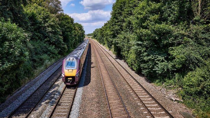 An intercity train moving approaching the viewer on one of four tracks bordered by trees, seen from slightly above