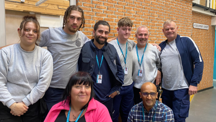 Eight people, staff and apprentices, lined up in front of a mock brick wall 