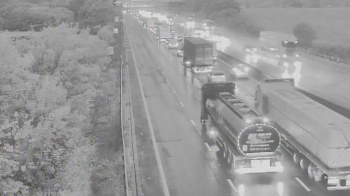 Traffic including cars and HGVs queued on the M25 motorway. The picture has been taken in the early hours of the morning and it is still dark outside.