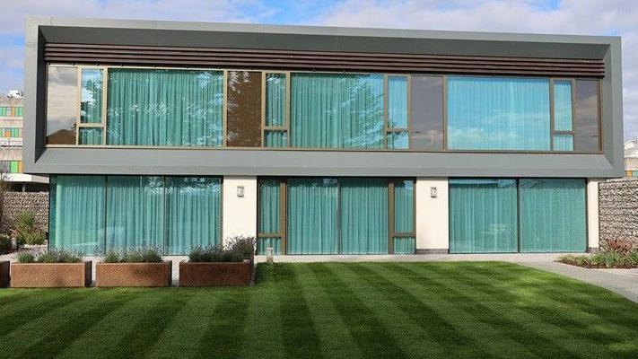 The new Maggie's centre in north Wales. It has a glass frontage and a well-kept lawn and gardens to the front. It sits on the site of Ysbyty Glan Clwyd, which can be seen in the background.