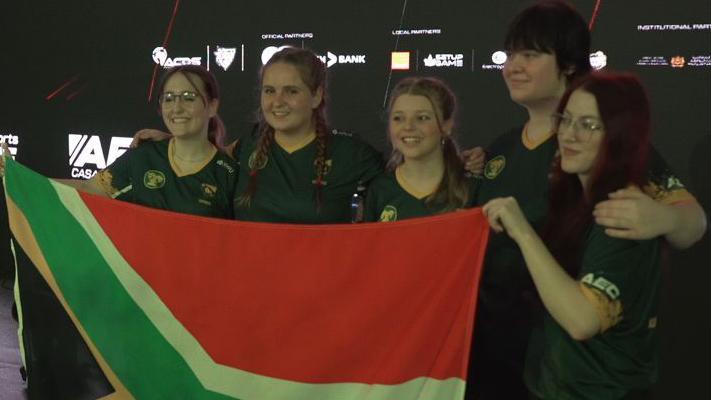 Five women pose for a picture and hold up a South African flag while celebrating a win at the African Esports Championship regional qualifier 2024